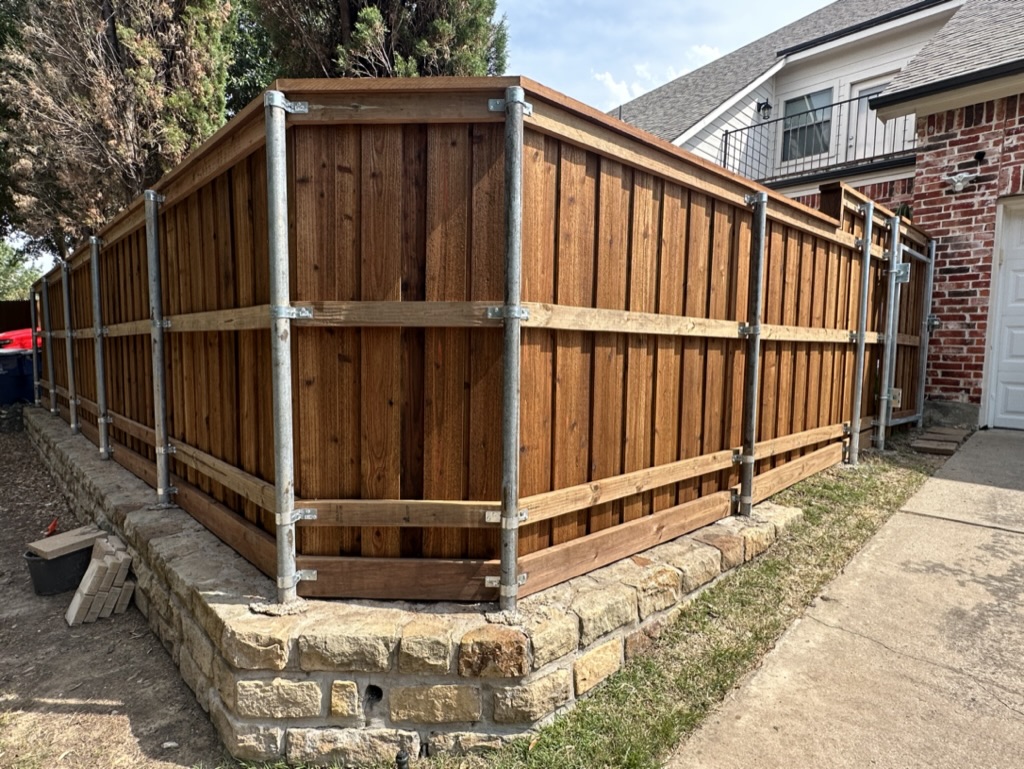 Board-on-board cedar fence with galvanized steel posts on a stone retaining wall