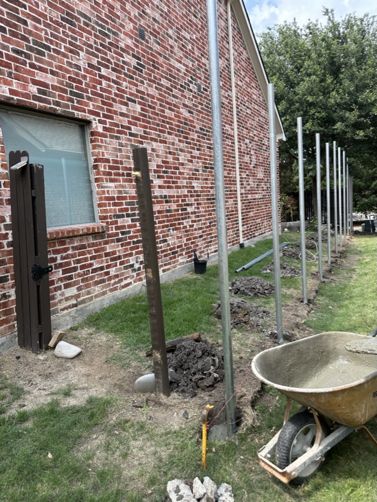 Galvanized steel fence post installation in progress along a brick home