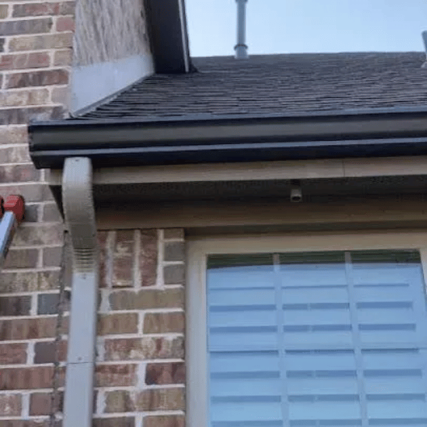 Newly installed seamless black gutters on a Rockwall brick home