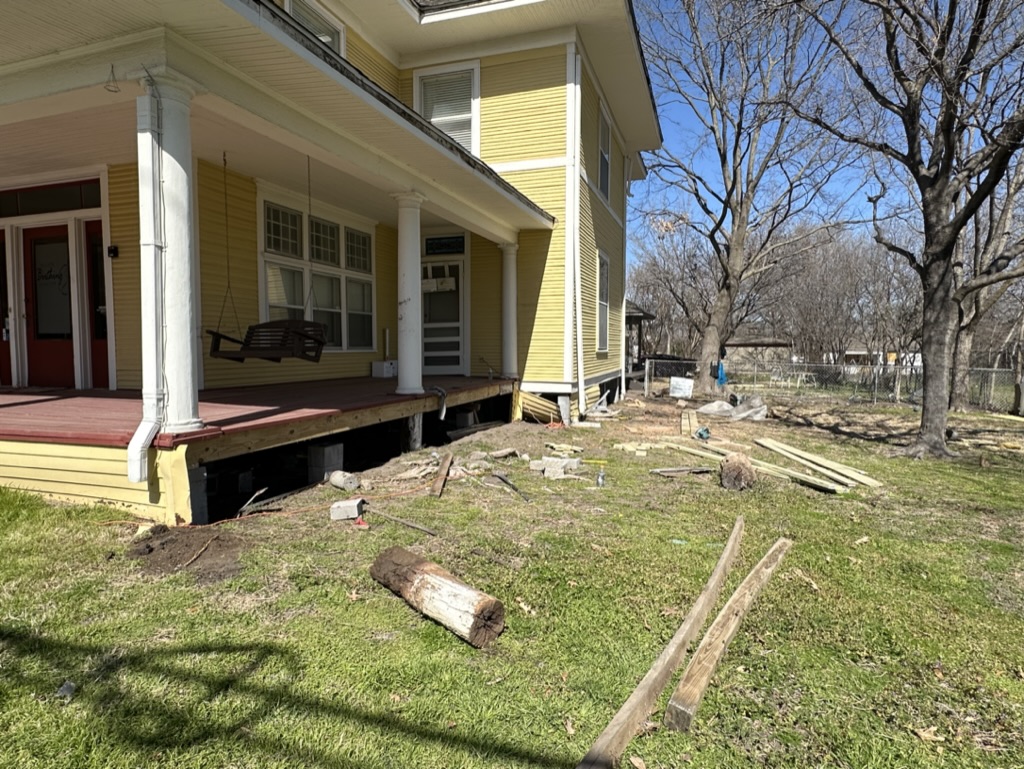 Foundation leveling and pier work in progress on a historic yellow farmhouse