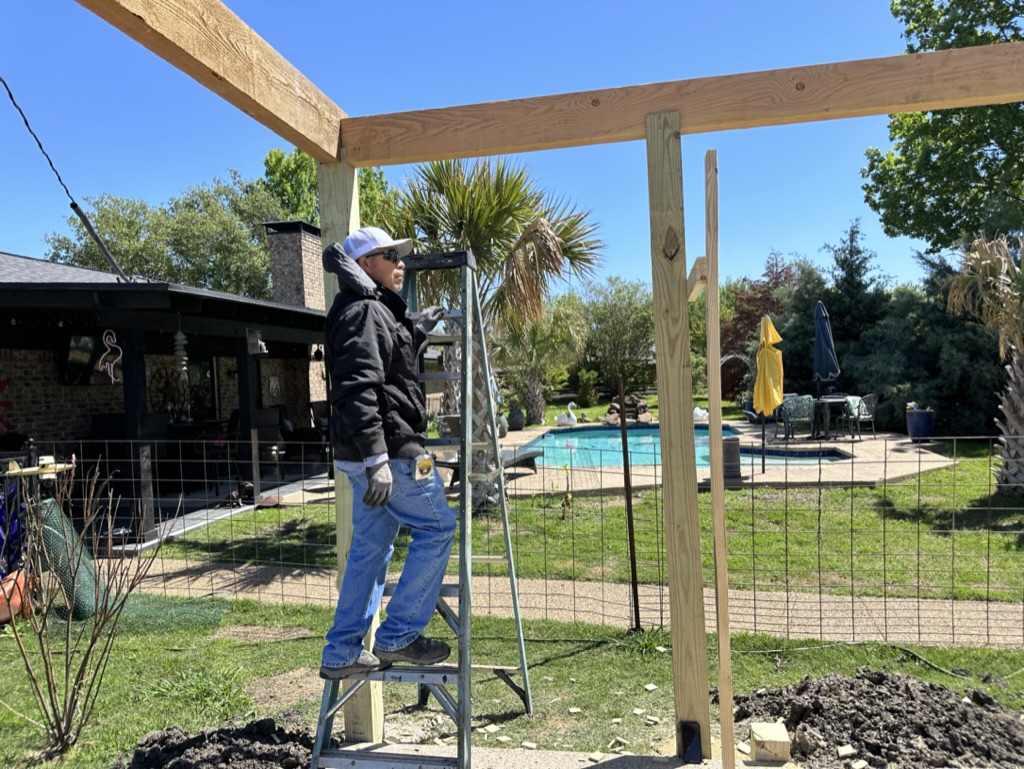 Cedar pergola framing being assembled near a backyard pool