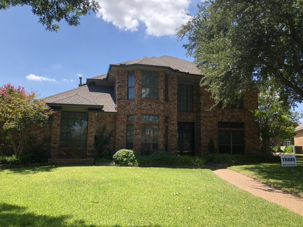 Completed shingle roof replacement on a two-story Rockwall brick home with Trake yard sign