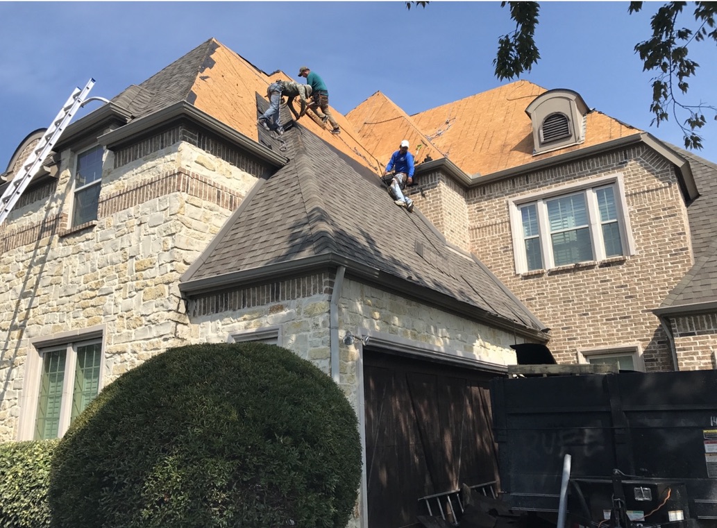 Trake Construction crew tearing off shingles on a stone and brick Rockwall home