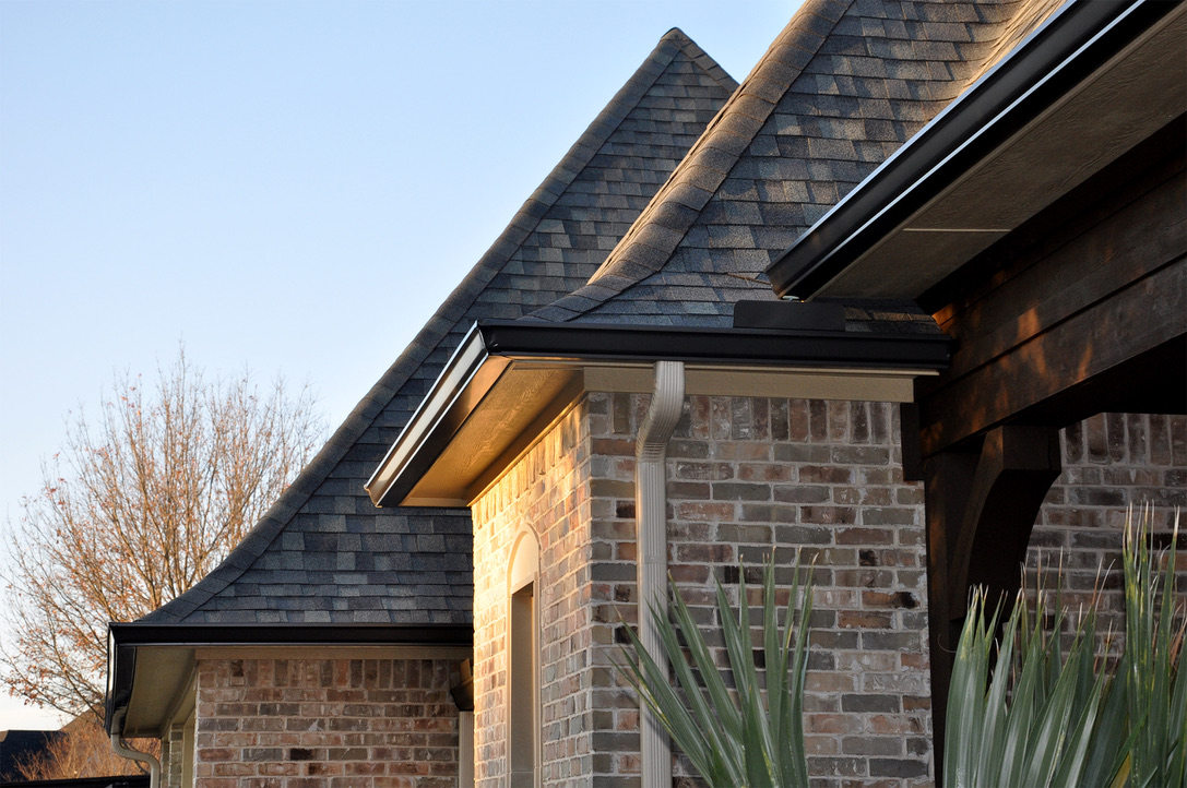 Close-up of new shingles, drip edge, and dark seamless gutters on a brick home