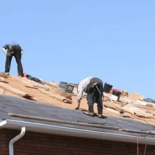 Roofing crew tearing off storm-damaged shingles to expose the decking for repair